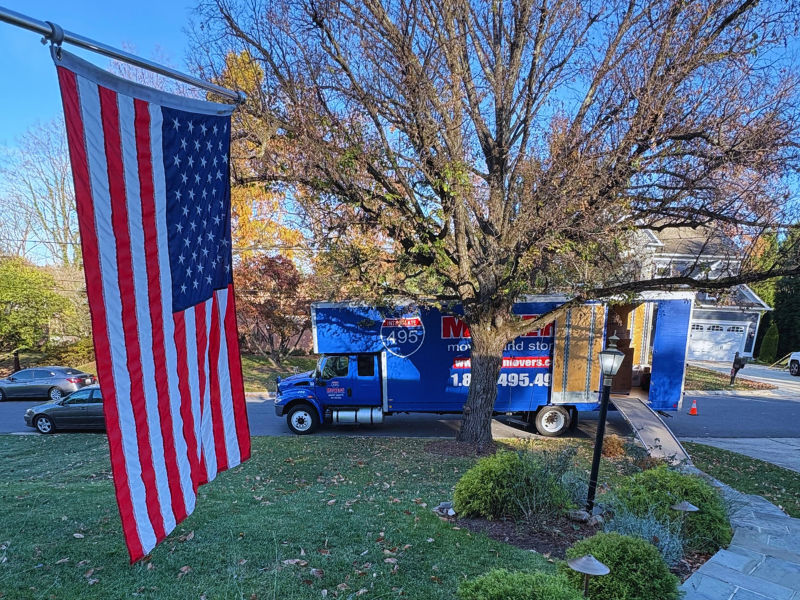 495 Movers truck parked outside house on street with an American flag in front